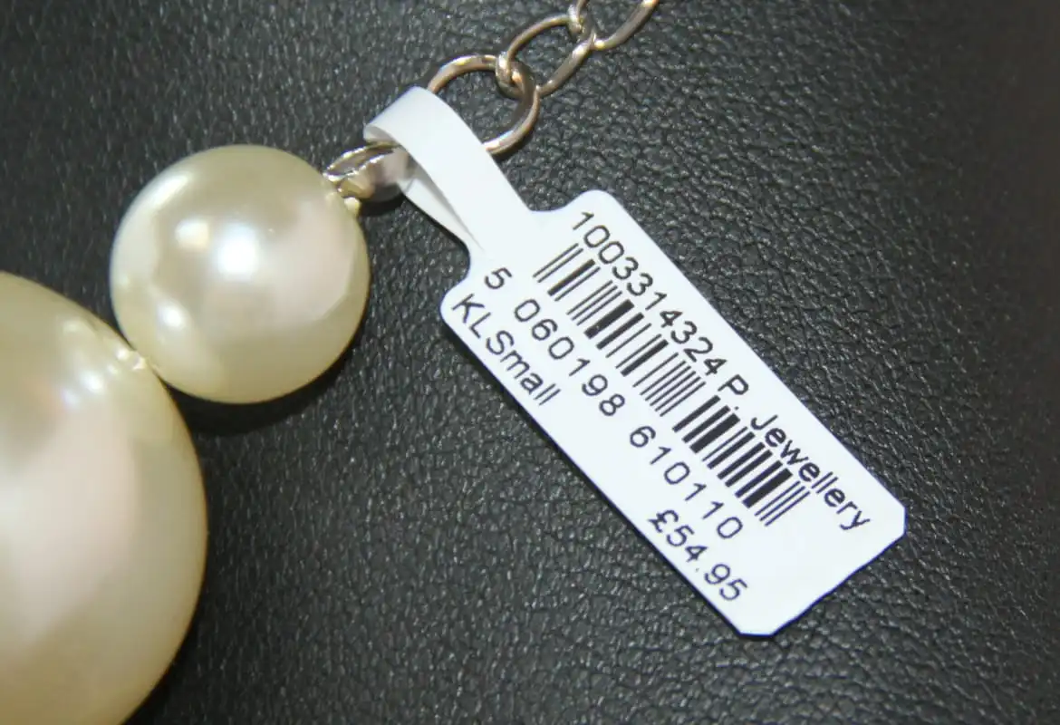 <p>GemTAGS barcode label printed price tag attached to a silver pearl chain necklace on a black surface</p>