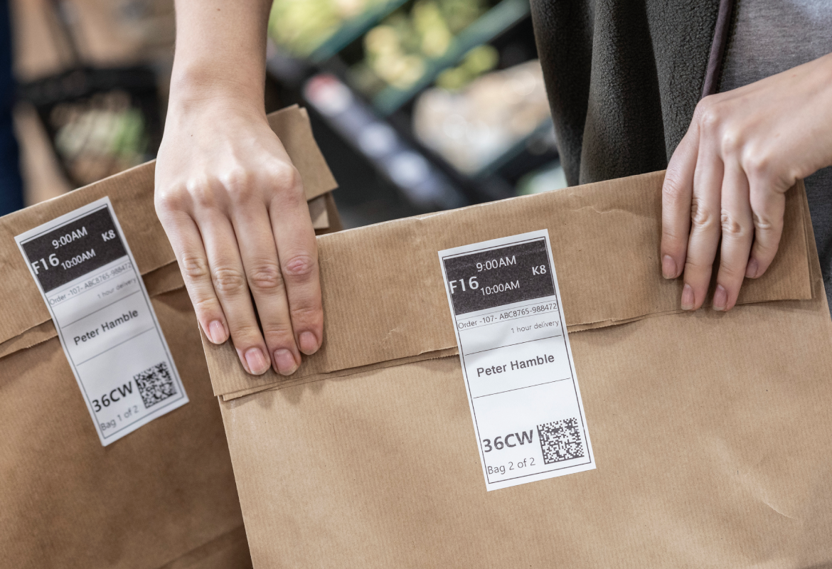 <p>Female hands securing Grocery click and collet bag with Printed order labels. </p>