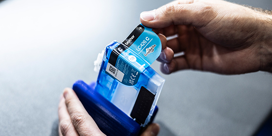 <p>A pair of hands applying a sticker to a blue Brother ink cartridge.</p>