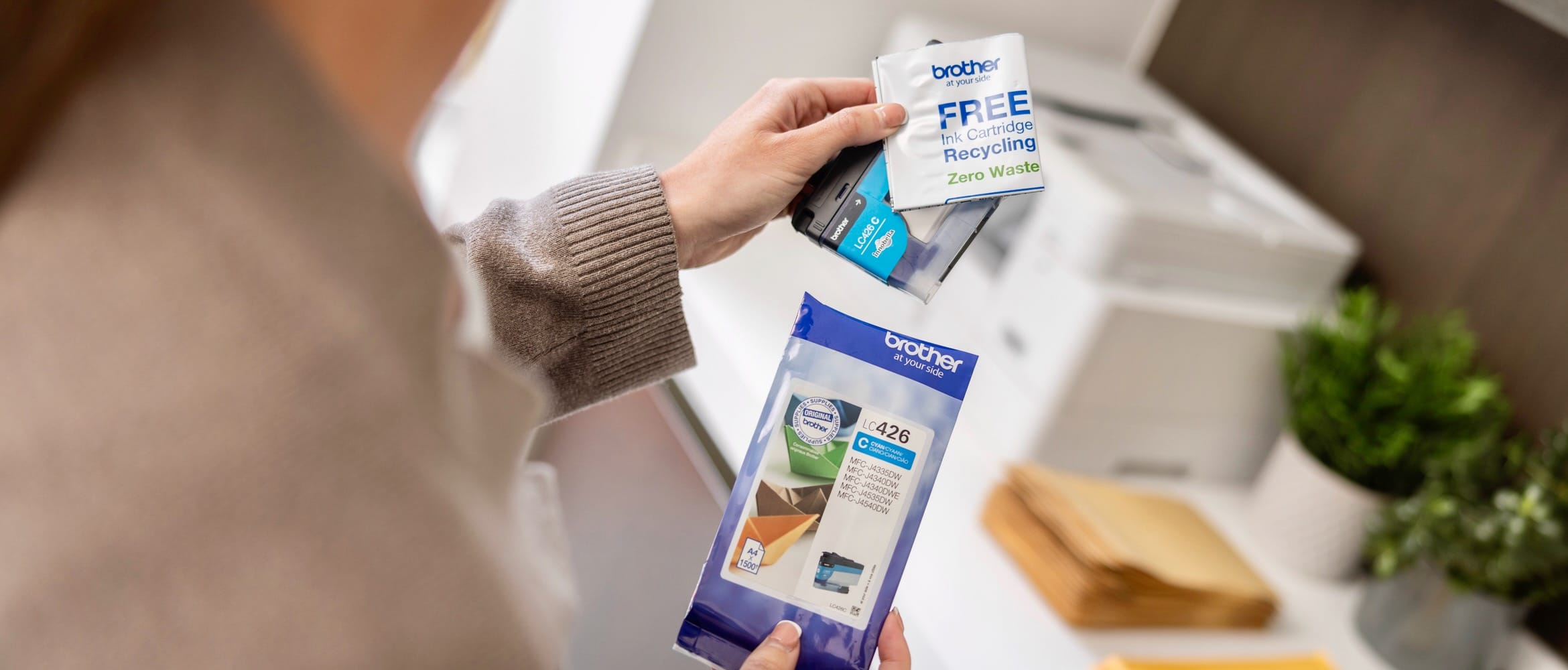 <p>Close-up of a lady holding a colour ink cartridge with free recycling return packaging in a home office environment</p>
