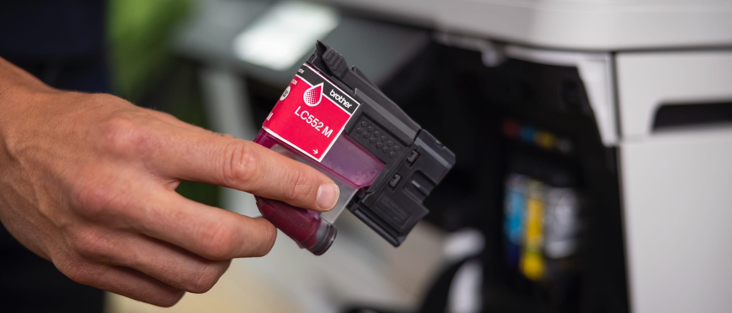 <p>Close-up of a man holding a magenta ink cartridge in front of a Brother inkjet printer</p>