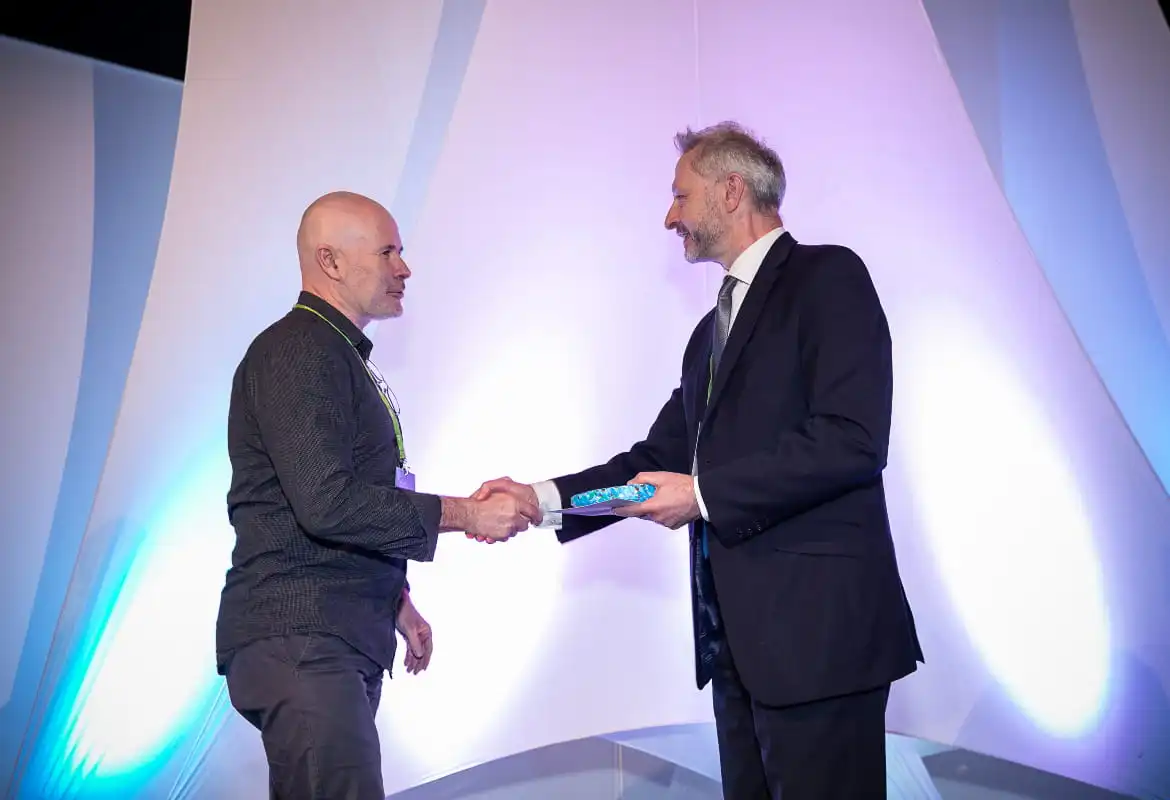 Two men stood shaking hands, with the man on the left accepting an award
