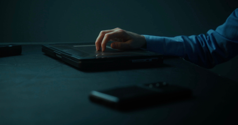 <p>Woman's hand placed on top of a laptop with a phone in the foreground</p>