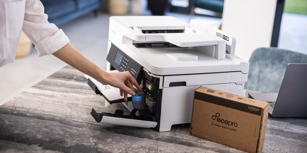 <p>Woman placing ink cartridge into printer on a table with an EcoPro box next to it</p>